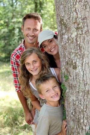 Smiling family standing behind a tree